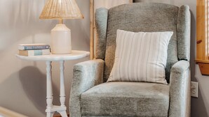 Un fauteuil gris avec un coussin à rayures, une table blanche avec une lampe et une pile de livres.
