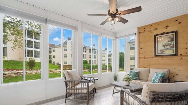 A sunroom with wicker furniture, large windows, and a ceiling fan. - Brookside Getaway | Spacious Sunroom (Branson)