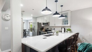 A modern kitchen with white cabinets, a central island, pendant lighting, and a clock on the wall. - Brookside Getaway | Spacious Sunroom (Branson)