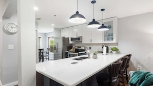 A modern kitchen with white cabinets, a central island, pendant lighting, and a clock on the wall. - Brookside Duo | Peaceful Views! (Branson)