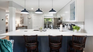 A modern kitchen with a central island, pendant lighting, and a view to a dining area. - Brookside Duo | Peaceful Views! (Branson)