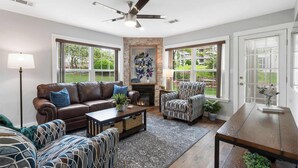 A spacious living room with a fireplace, leather sofa, patterned armchairs, and a dining table. - Brookside Duo | Peaceful Views! (Branson)