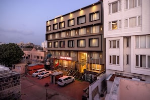 A hotel with multiple floors, a visible staircase, and a parking area with several cars. - Manek the Ocean View (Dwarka)