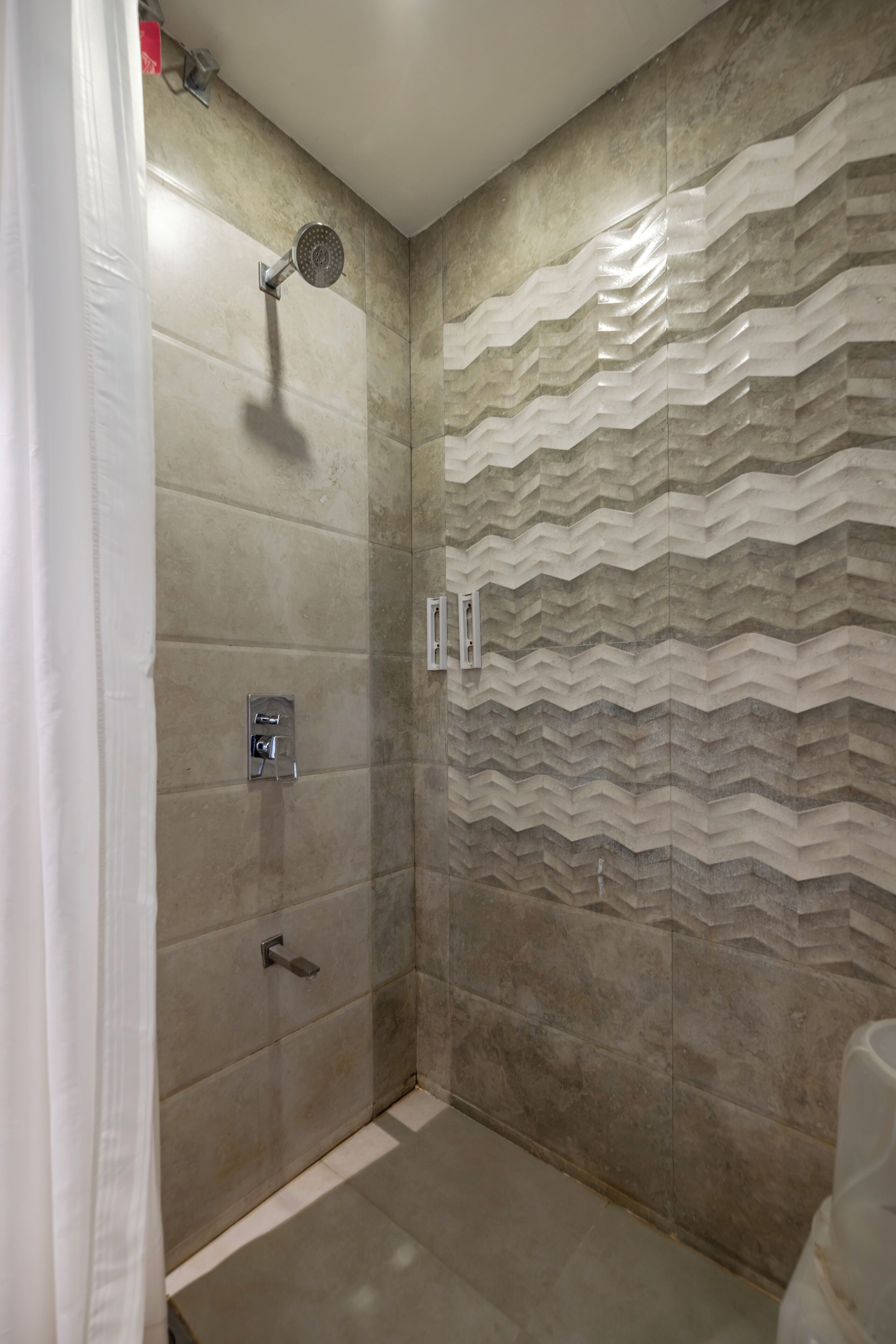 A shower with a handheld showerhead, a control panel, and a wall-mounted faucet.