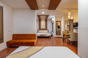 A hotel room with a bed, a sofa, a desk, and a dining area. - Manek the Ocean View (Dwarka)