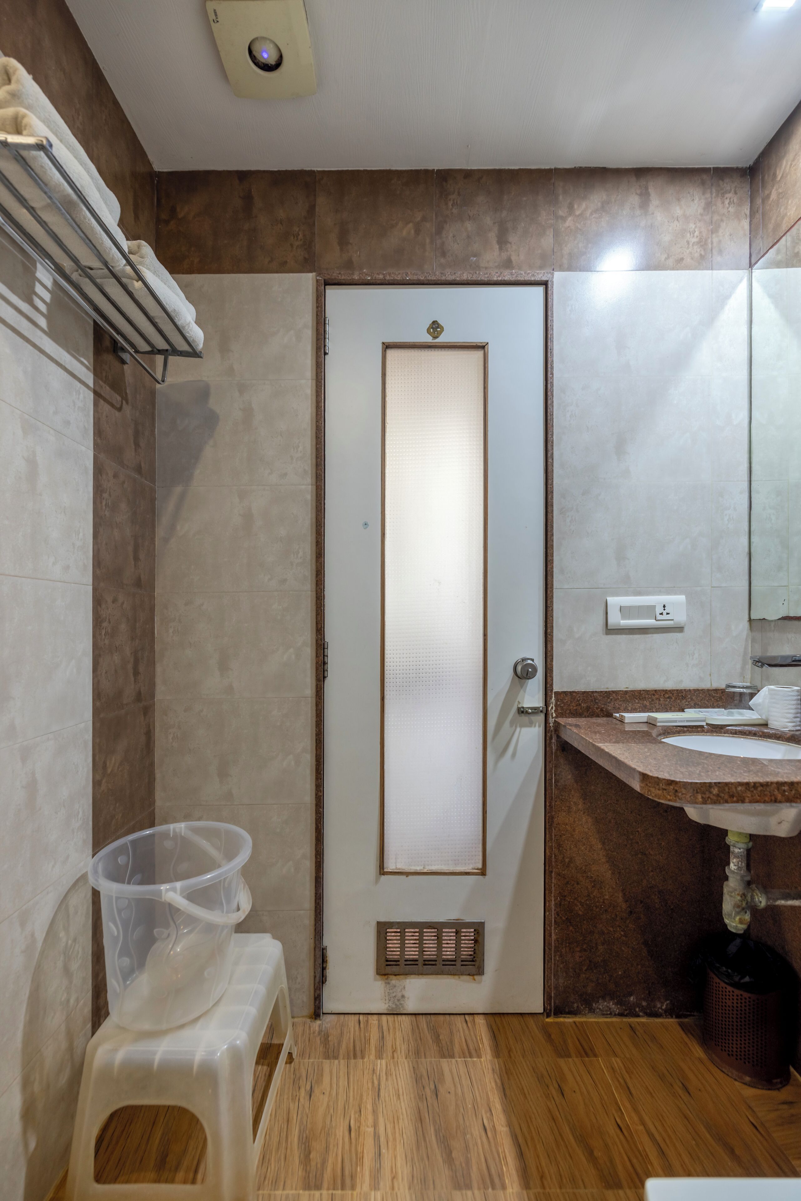 A bathroom with a wooden floor, a white door, a sink with a mirror, and a towel rack.