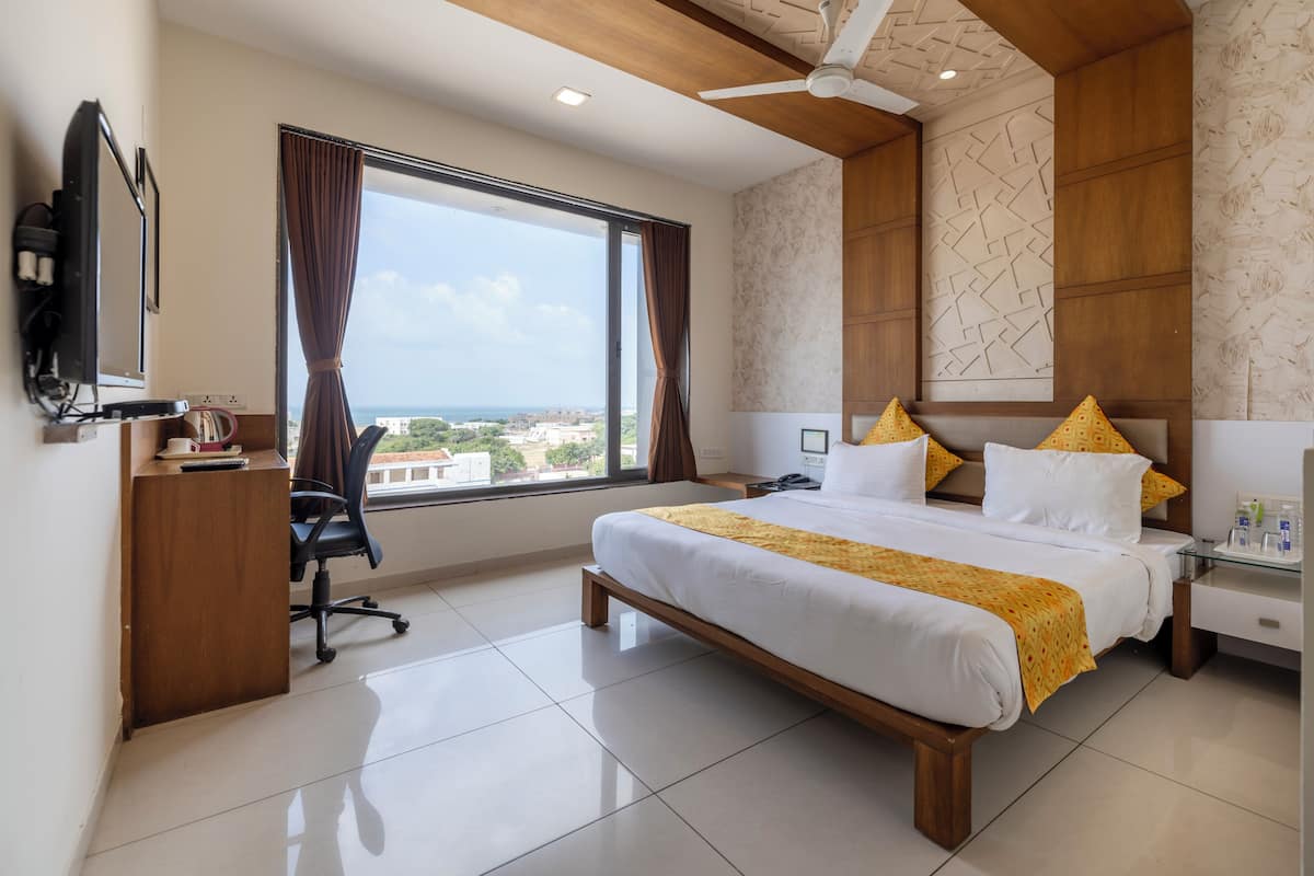 A hotel room with a large bed, a desk, a chair, a TV, and a view of the city.