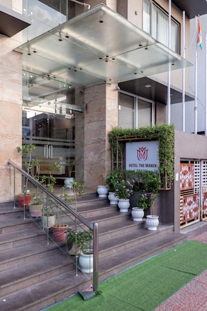 A hotel entrance with a glass canopy, steps, potted plants, and a signboard. - Manek the Ocean View (Dwarka)