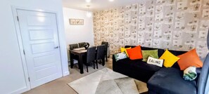 A living room with a black sofa, a dining table with chairs, and a patterned wallpaper. - Cozy Peace in Sittingbourne (Sittingbourne)