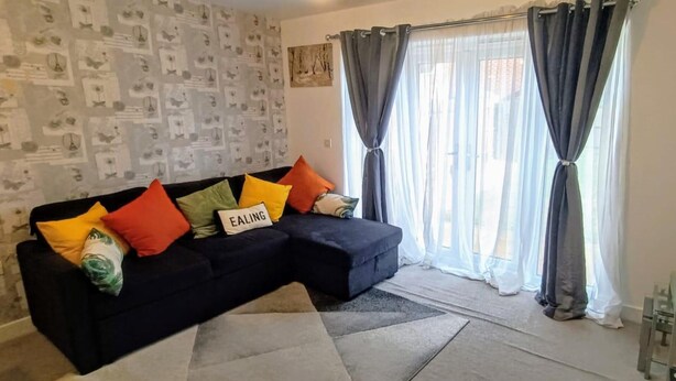 Ein Wohnzimmer mit einem dunkelgrauen Sofa, mehreren bunten Kissen, einem Glastisch und einem Gemälde an der Wand.
