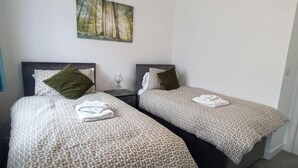 Ein Hotelzimmer mit zwei Betten, jeweils mit gemusterten Bettdecken und Kissen, einem kleinen Nachttisch mit Lampe und einem Bild an der Wand.