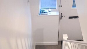 Eine Treppe mit Teppichstufen, weißen Geländern und einem kleinen Fenster am Oberende.