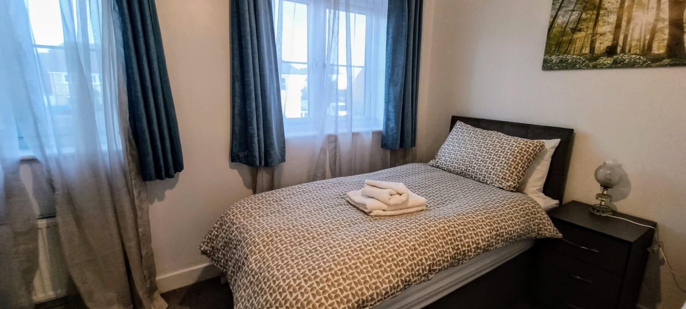 A bedroom with a bed, a nightstand, and a window with curtains.
