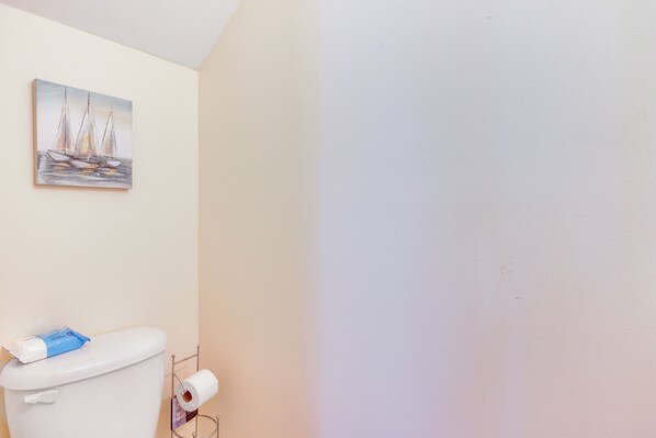 A bathroom with a toilet, a roll of toilet paper, and a painting of sailboats on the wall. - Modern Gem: 18 Mi to Downtown Columbia! (Elgin)