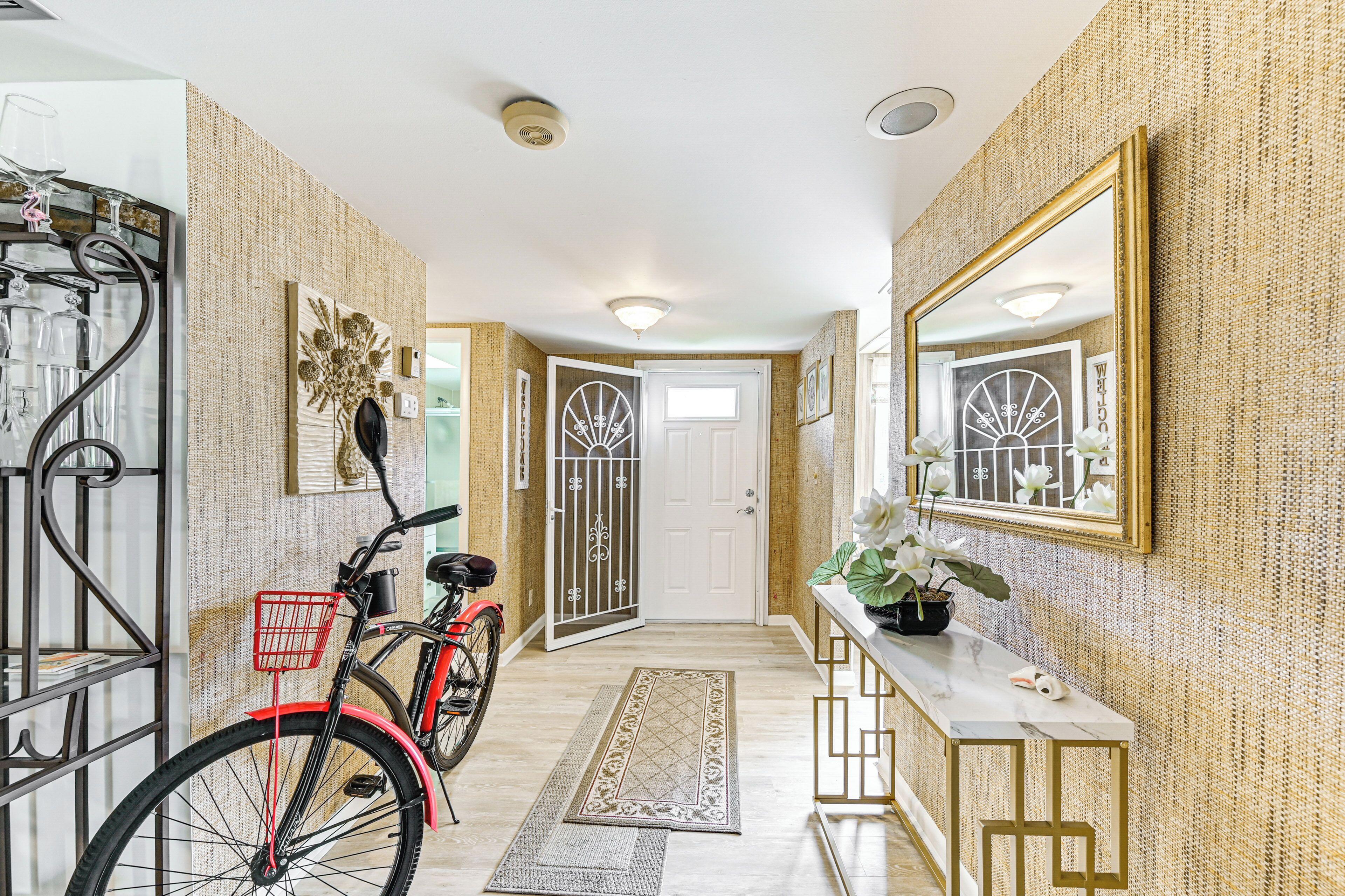 A hallway with a bicycle, a console table with a plant, and a mirror on the wall.