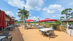 An outdoor patio with tables and chairs, red umbrellas, and a wooden deck. - 3 Mi to Downtown Naples: Country Club Condo! (Naples)
