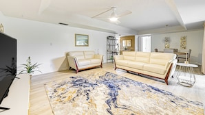 A spacious living room with two cream-colored sofas, a large abstract rug, and a ceiling fan. - 3 Mi to Downtown Naples: Country Club Condo! (Naples)