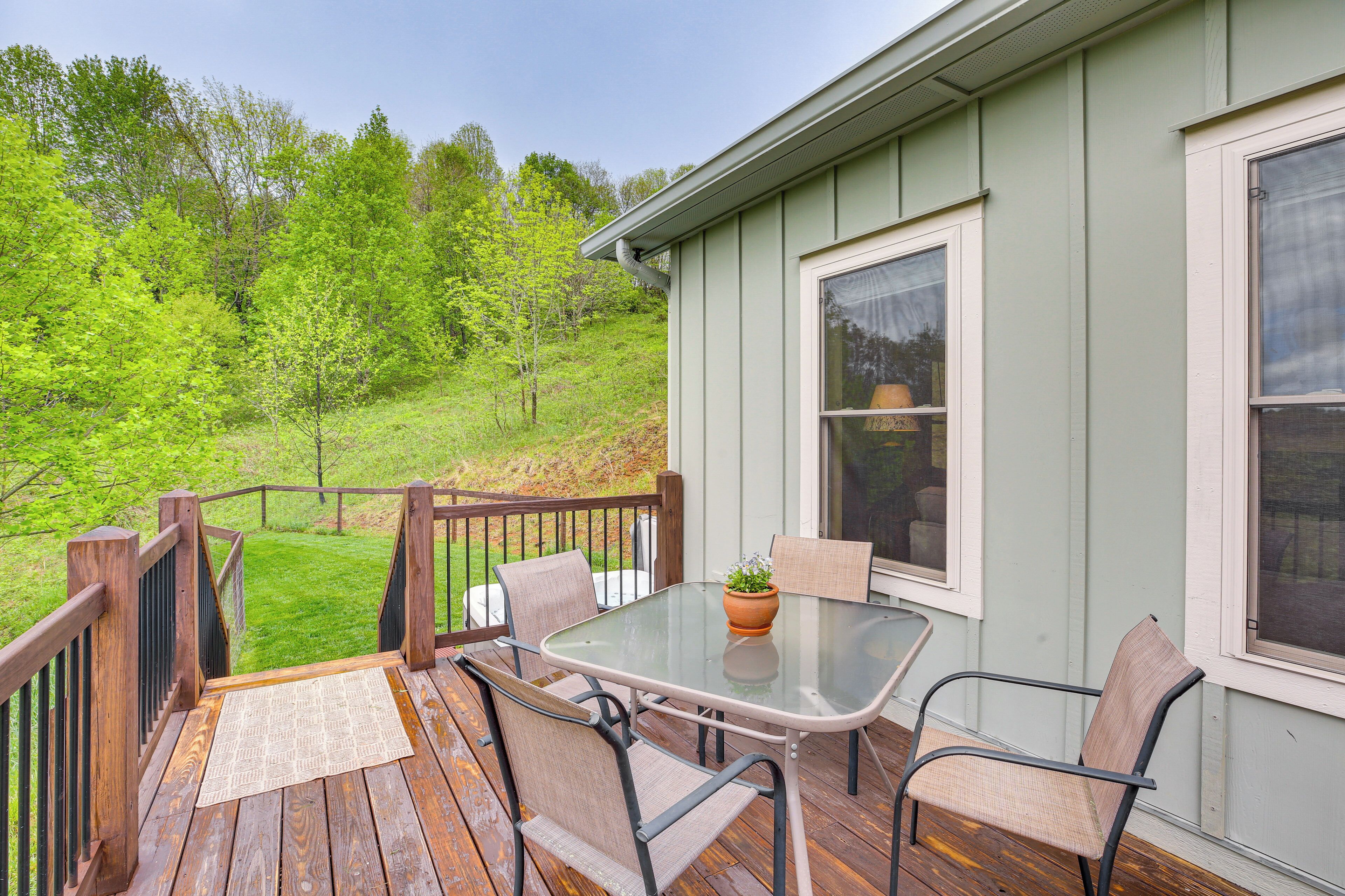 A deck with a glass table and chairs, a potted plant, and a view of a green landscape.