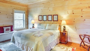 Un dormitorio con paneles de madera, una cama, lámparas de noche, un banco y cuadros en la pared.