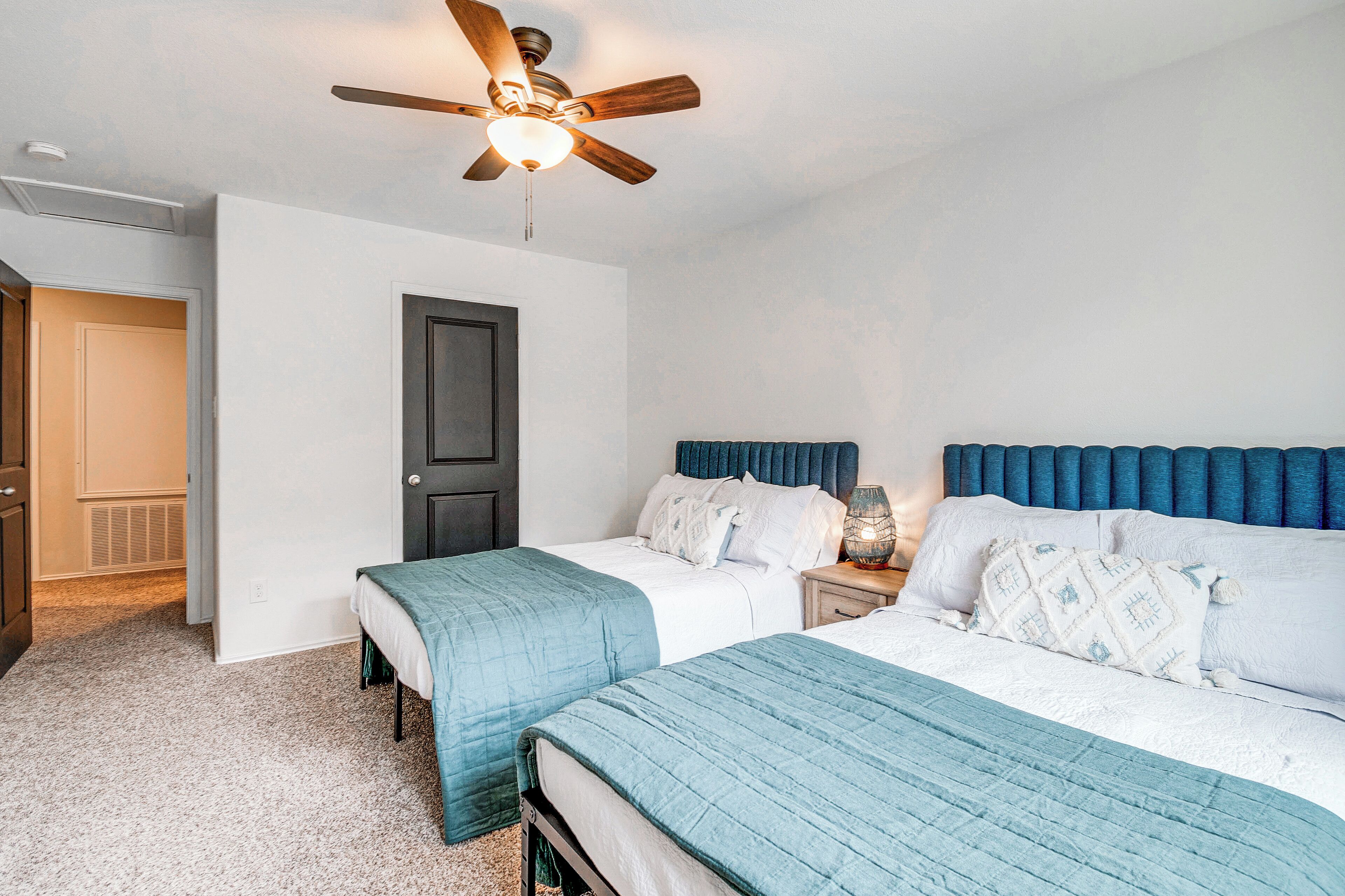 A bedroom with two beds, a ceiling fan, a nightstand with a lamp, and a door.