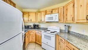Una cocina con armarios de madera, un refrigerador blanco, un microondas, una estufa y una encimera de granito.
