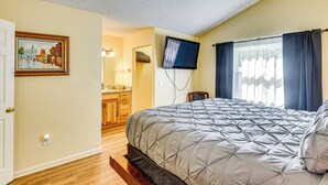 Un dormitorio con una cama, un televisor montado en la pared y un ventanal con cortinas.