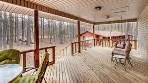 A covered wooden deck with a table and chairs, overlooking a forested area and a red building. - Heber Springs Cabin w/ Deck: 3 Mi to Sugarloaf Mtn (Heber Springs)