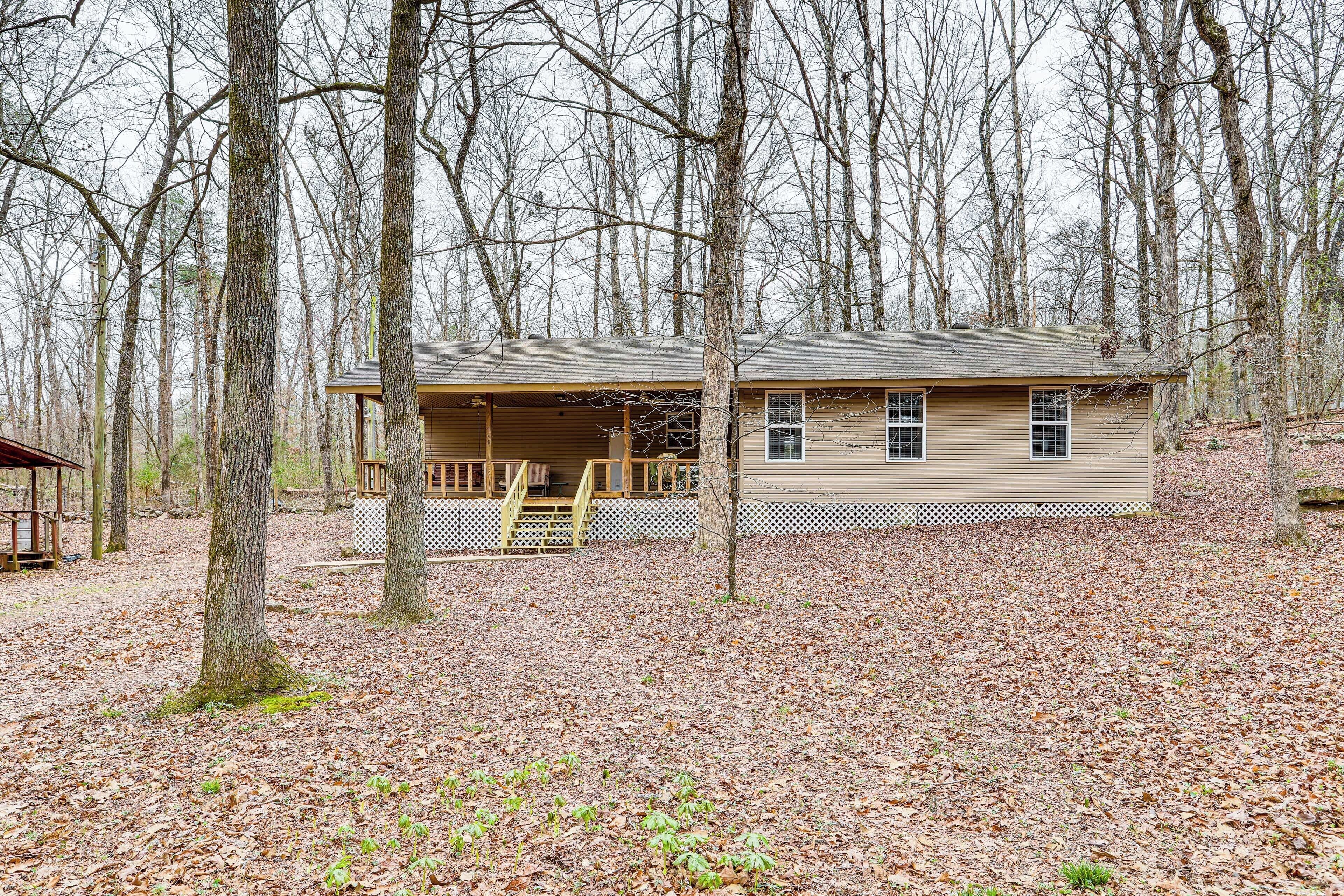 A single-story house with a porch, surrounded by a wooded area.