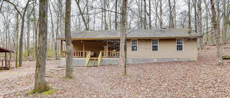 A single-story house with a porch, surrounded by a wooded area.