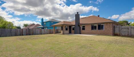 A residential property with a brick house, a wooden fence, and a clear blue sky.