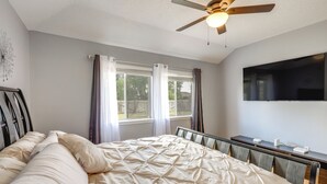 Une chambre avec un lit, un bureau, un ventilateur de plafond et un téléviseur fixé au mur.