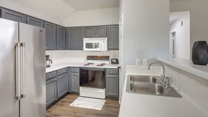 Une cuisine moderne avec des meubles gris, un réfrigérateur en acier inoxydable, un four à micro-ondes blanc et un évier à deux bacs.