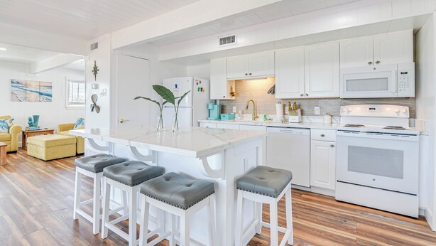 A modern kitchen with white cabinetry, a central island with stools, and a built-in oven and microwave. - Enjoy the View, Walk to Beach! Galveston Hideaway (Galveston)