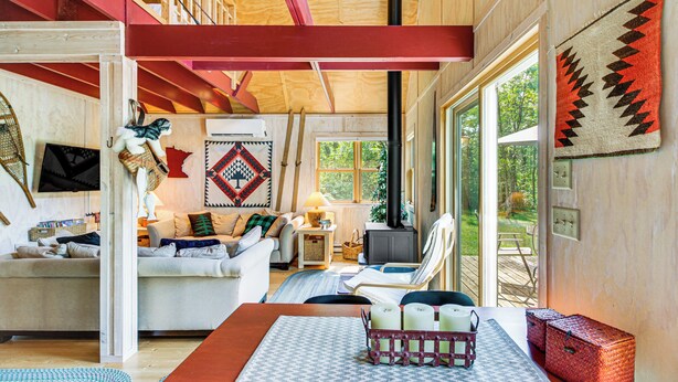A cozy cabin interior with a fireplace, a sofa, a dining table, and a large window offering a view of the outdoors. - Riverside Retreat in Crosby: Pet Friendly! (Crosby)