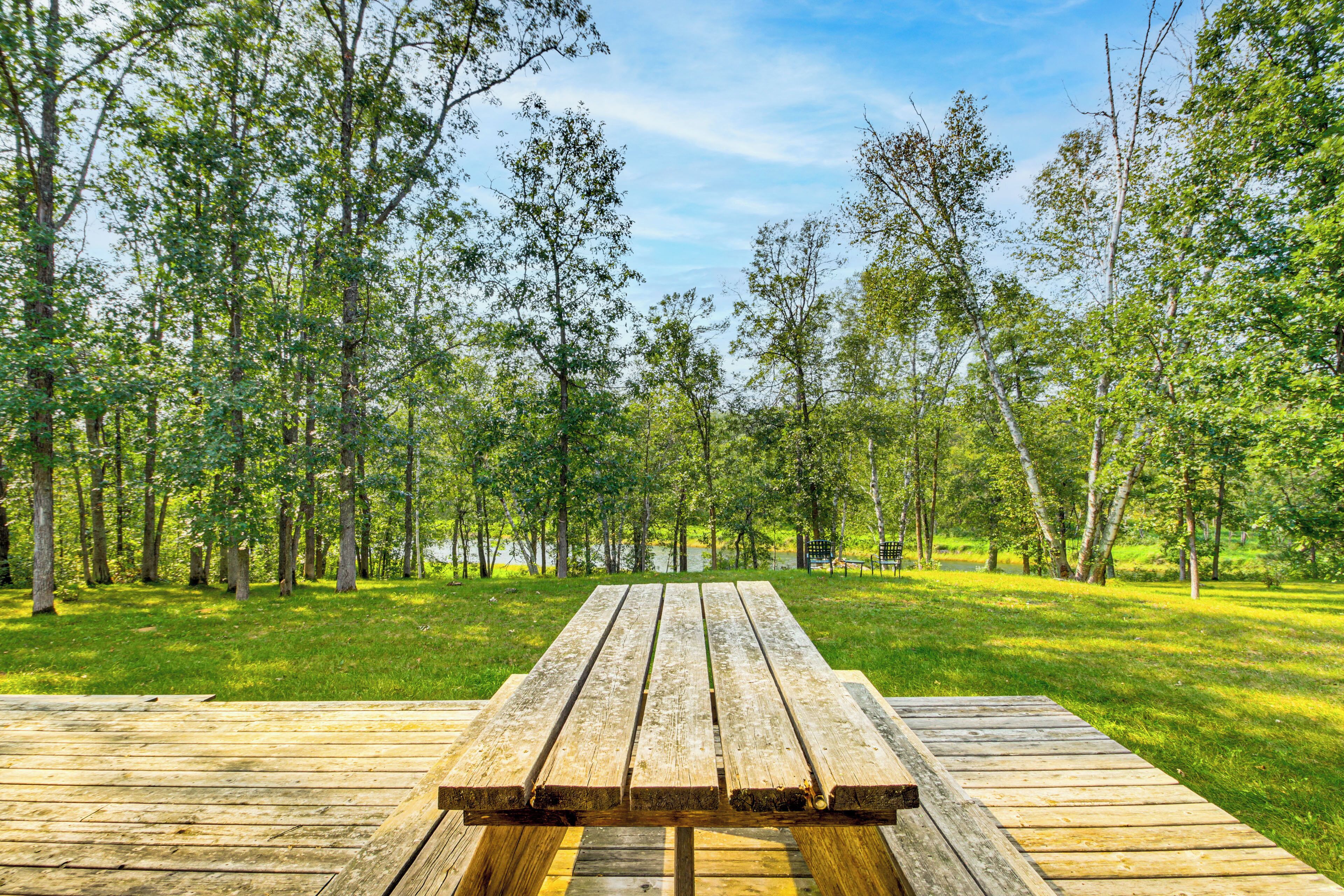 A wooden picnic table in a grassy park with trees in the background.