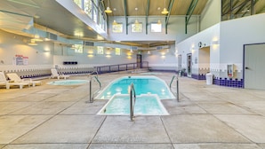 Una piscina interior con sillones de descanso, una escalera y vistas al cielo a través de grandes ventanales.