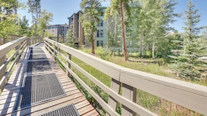 Un puente peatonal de madera con rejas metálicas, rodeado de árboles y edificios.