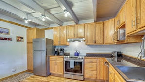Una cocina con gabinetes de madera, un refrigerador de acero inoxidable, un horno, un microondas y un fregadero.