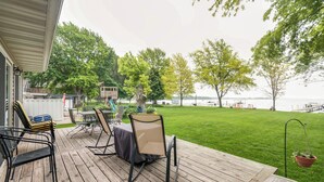 A wooden deck with outdoor furniture, a grassy lawn, and a view of the water.