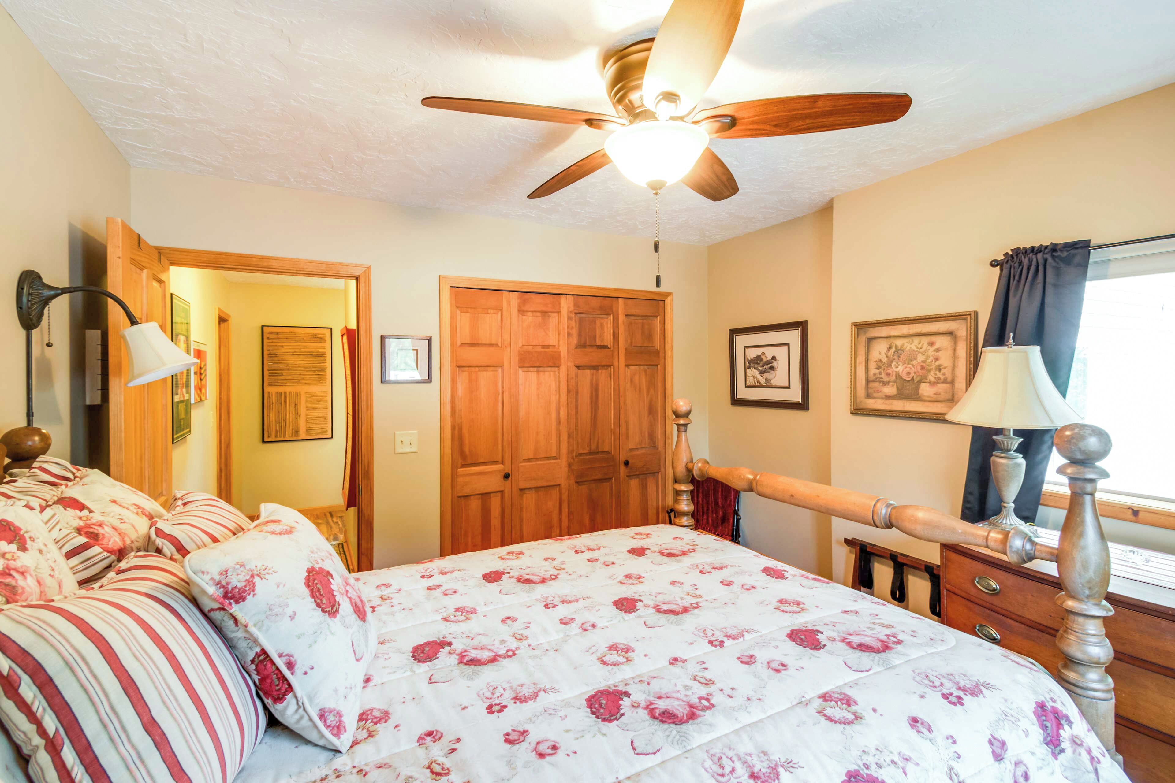 A bedroom with a bed, a ceiling fan, a wooden door, and a dresser.