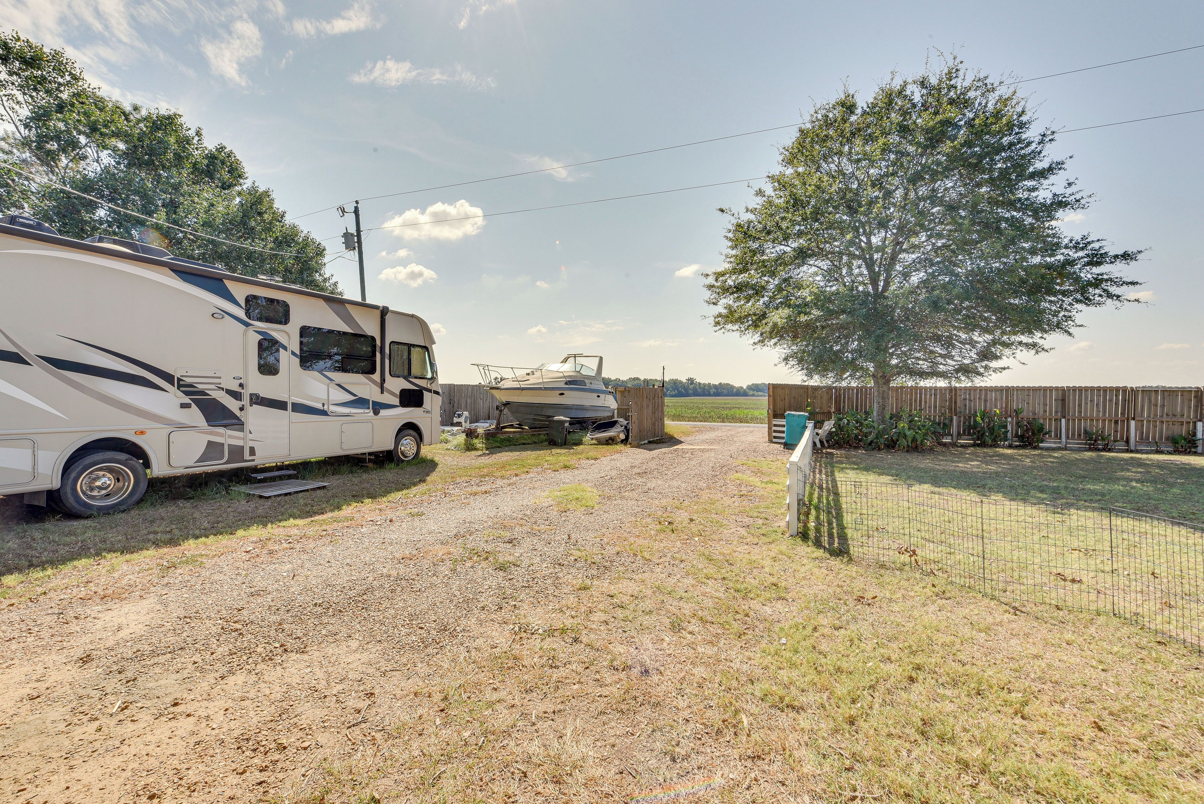 A recreational vehicle (RV) parked on a gravel path with a wooden fence and trees in the background.