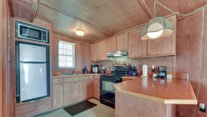 A compact kitchen with wooden cabinets, a microwave, a refrigerator, a stove, and a coffee maker. - Waterfront Jonesville Studio on Black River Lake! (Jonesville)