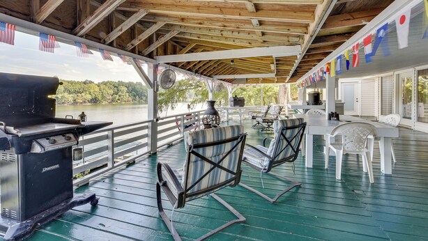 A covered outdoor deck with a grill, chairs, and a view of a lake. - Waterfront Jonesville Studio on Black River Lake! (Jonesville)