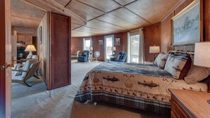 A spacious bedroom with a large bed, a desk, and a chair. There is a door leading to another room, and a window providing natural light. - Waterfront Jonesville Studio on Black River Lake! (Jonesville)