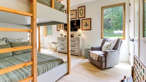 Una camera da letto con un letto a castello, una poltrona grigia, un comò in legno e quadri appesi al muro.