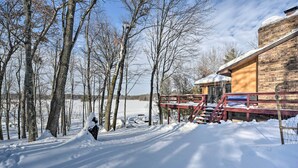 A snow-covered landscape with a wooden cabin and a red staircase leading to a deck. - Snowmobile, Ice Fish & Explore! Lang Lake Cabin (Danbury)