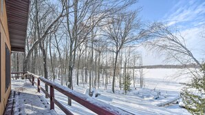 A wooden deck with a red railing overlooking a snow-covered landscape with trees and a clear sky. - Snowmobile, Ice Fish & Explore! Lang Lake Cabin (Danbury)