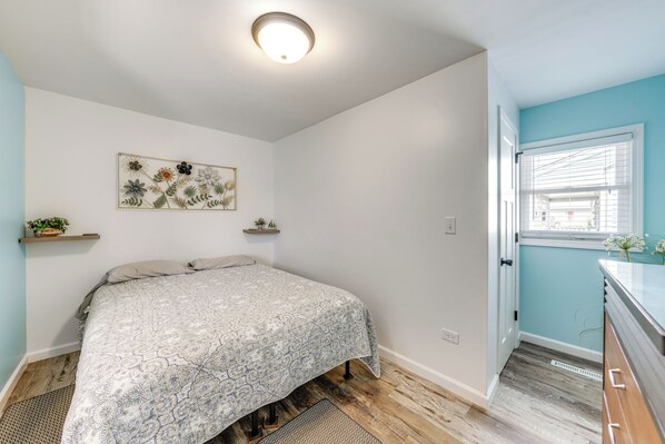 A bedroom with a bed, a ceiling light, a wall-mounted artwork, and a window with blinds.