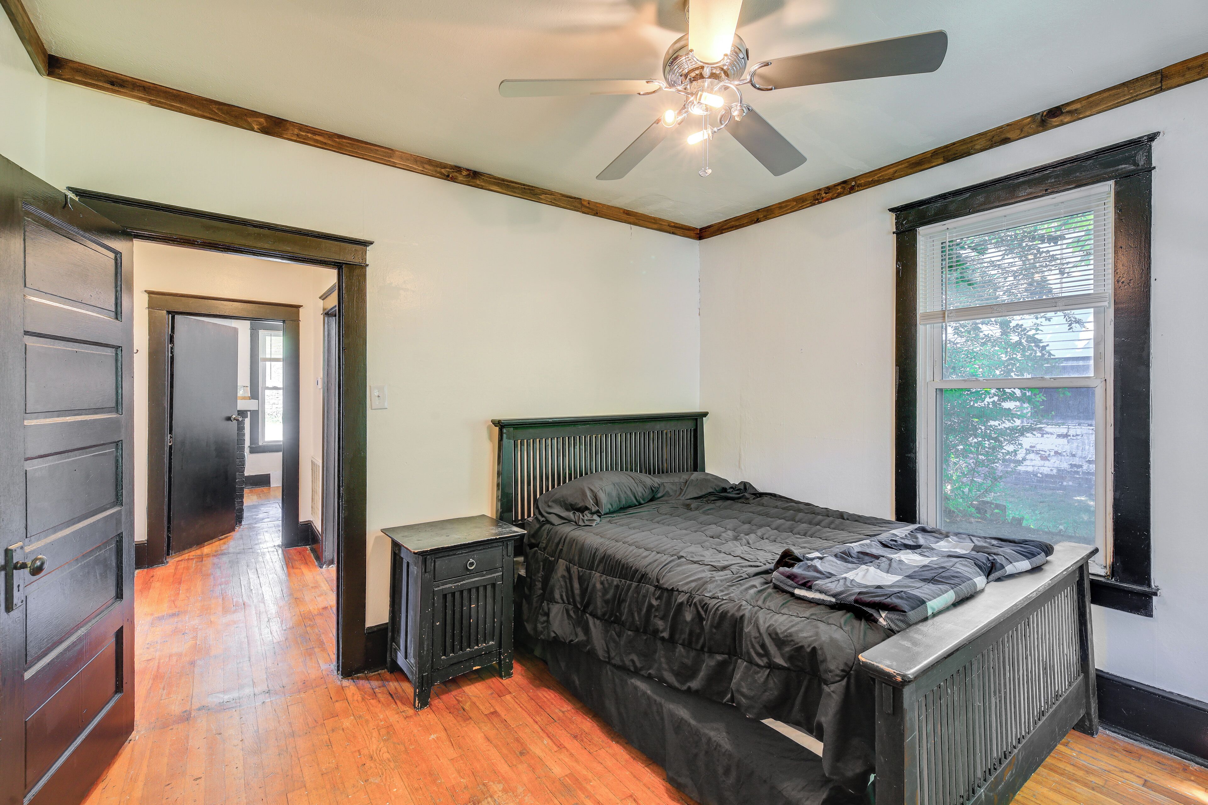 A bedroom with a bed, a nightstand, a ceiling fan, and a window.