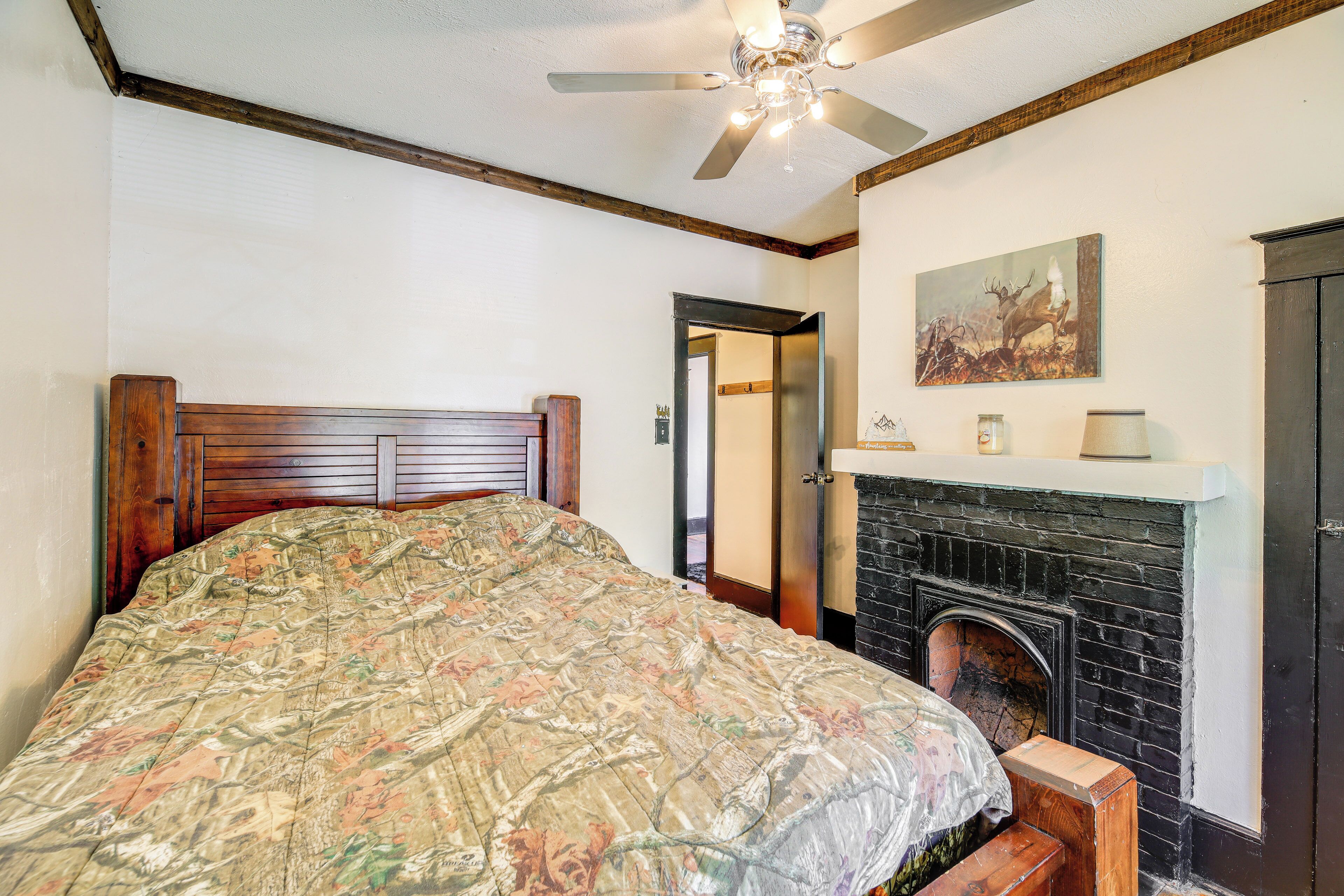 A bedroom with a wooden headboard, a large floral bedspread, a fireplace, and a ceiling fan.